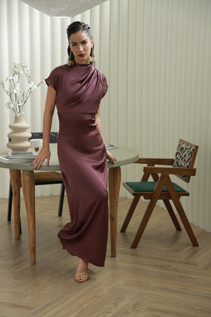Woman in a long burgundy dress standing in a room with wooden furniture and decor.